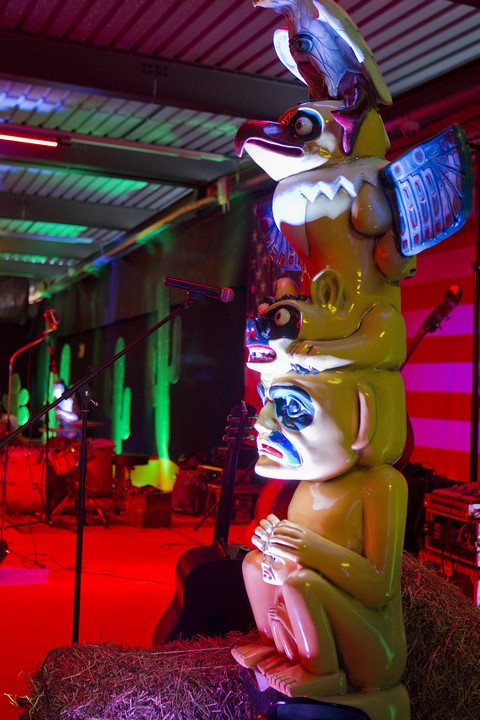 Sculpture totem colorée éclairée par des lumières de scène, présentée à côté d'un microphone sur une scène avec de la paille au sol, suggérant une décoration thématique pour un événement western.